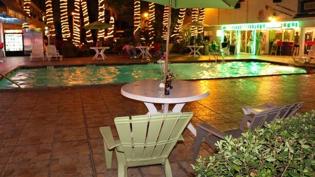 An outdoor pool area with a table and chairs, surrounded by a patio with a tiled floor.
