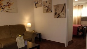 Une pièce comprenant un canapé, une petite table avec une lampe et un lit recouvert d’une couvre-lit à motifs floraux. Des tableaux représentant des fleurs sont accrochés aux murs.
