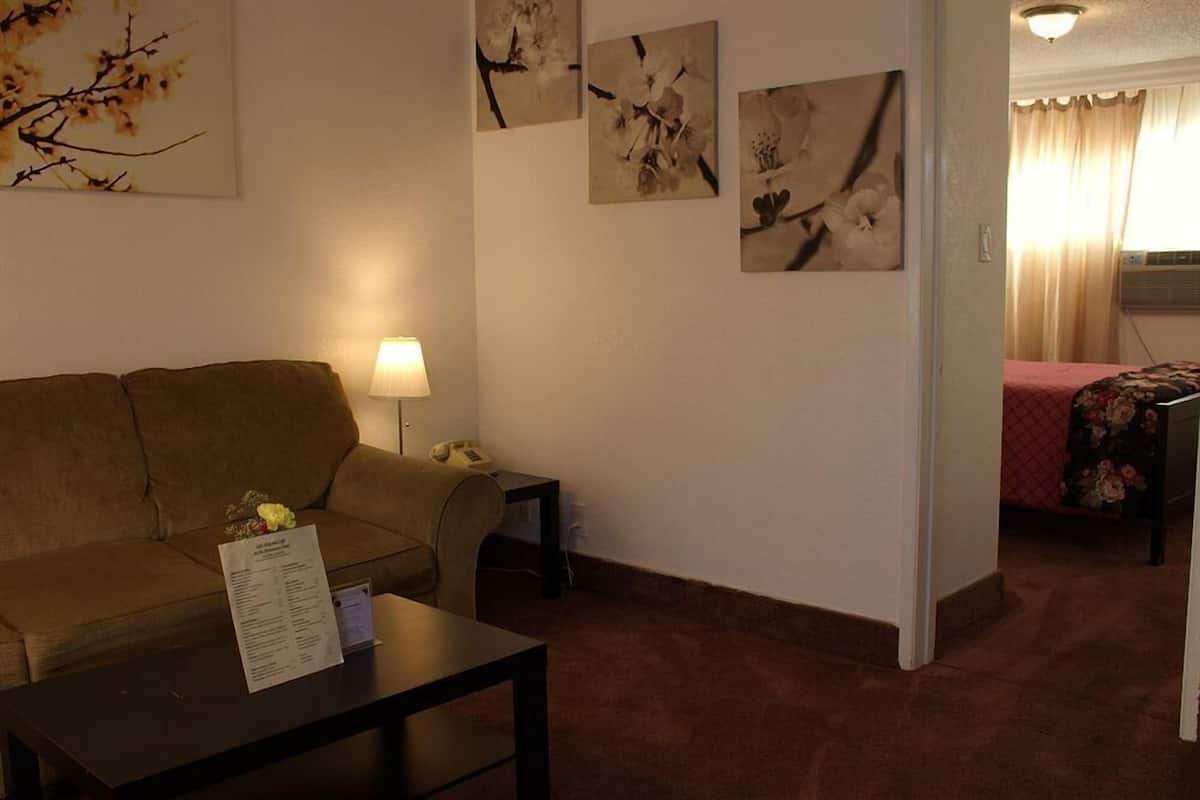 A room with a sofa, a small table with a lamp, and a bed with a floral bedspread. There are wall-mounted pictures of flowers.