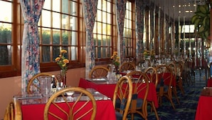 Un restaurant avec de longues tables, des chaises en bois et des rideaux à motifs floraux.