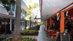 A narrow outdoor corridor with a tree and flower beds, a staircase, and a restaurant with outdoor seating.
