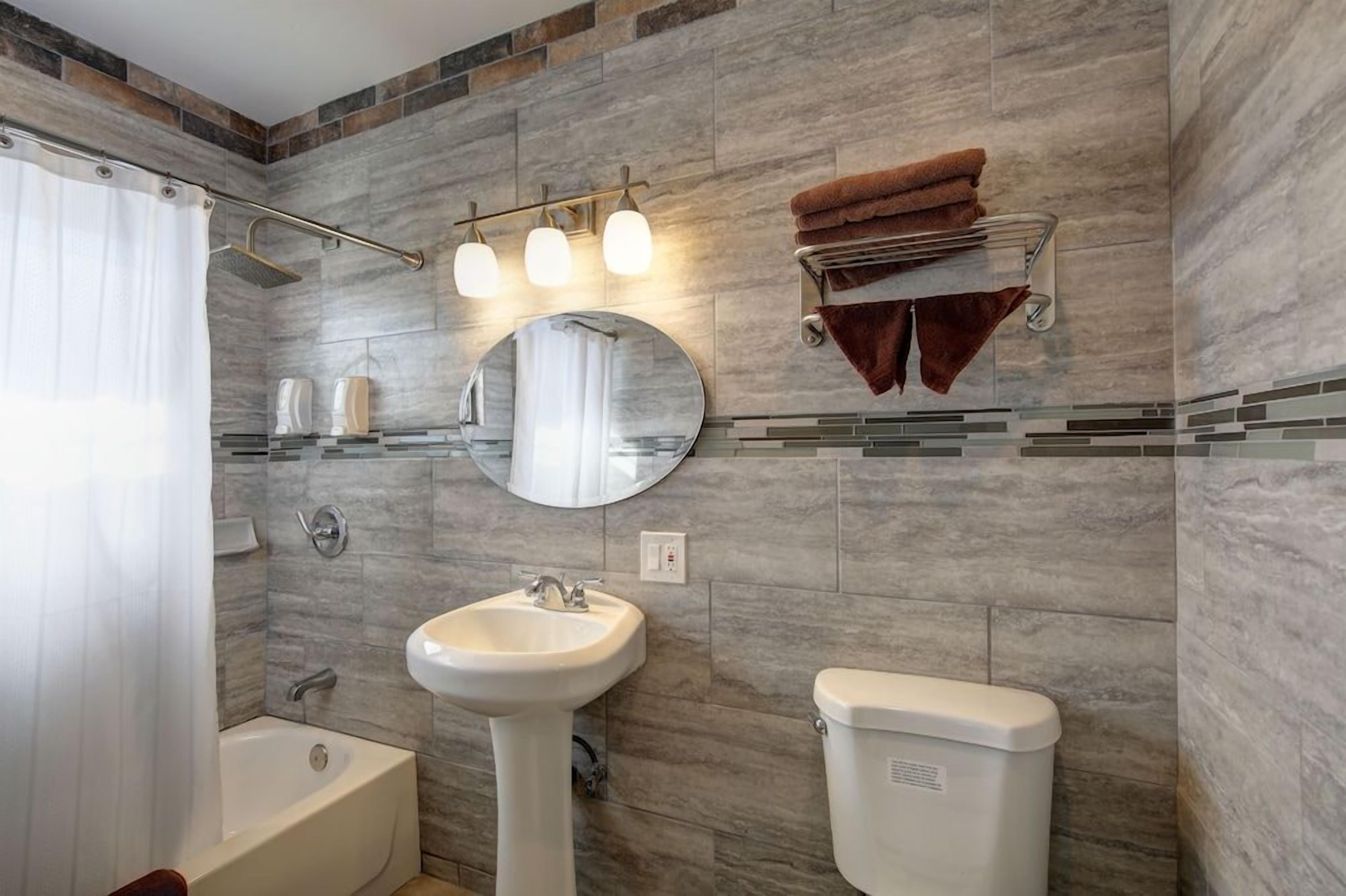 Un baño con bañera, lavamanos e inodoro, que presenta una pared de piedra y un perchero para toallas.