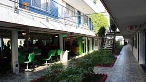 A covered outdoor seating area with green chairs and tables, a small garden, and an exit sign.