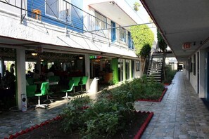 A covered outdoor seating area with green chairs and tables, a small garden, and an exit sign. - Tradewinds All Suite Hotel (Inglewood)
