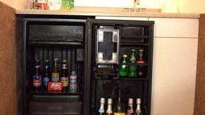 Un réfrigérateur compact doté d’un compartiment congélateur à gauche et d’un compartiment principal à droite, contenant diverses boissons et condiments.