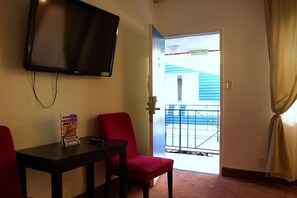 A room with a television mounted on the wall, a table with a chair, and a view of a balcony with a railing. - Tradewinds All Suite Hotel (Inglewood)