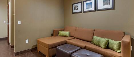 A modern living room with a sectional sofa, a matching ottoman, and a wall with framed pictures.