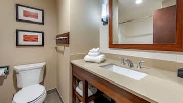 Un baño con inodoro, lavabo y espejo. Hay dos cuadros enmarcados en la pared.