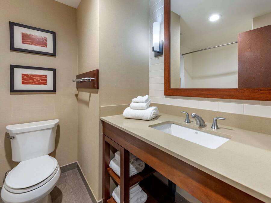 A bathroom with a toilet, sink, and mirror. There are two framed pictures on the wall.