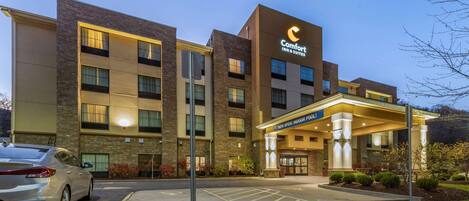 A Comfort Inn & Suites hotel with a modern design, featuring a well-lit entrance and a parking area.