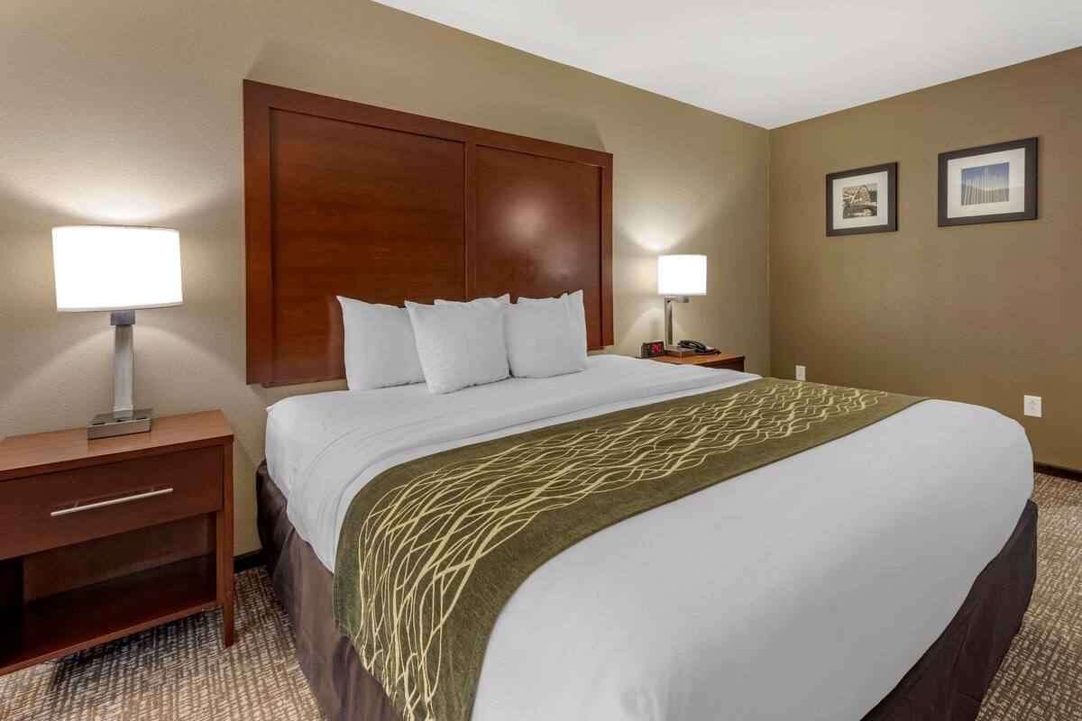 A hotel room with a large bed, two bedside tables, a wooden headboard, and two wall-mounted lamps.