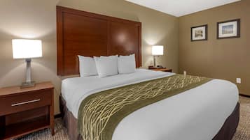 Una habitación de hotel con una cama grande, dos mesitas de noche, un cabecero de madera y dos lámparas fijadas a la pared.
