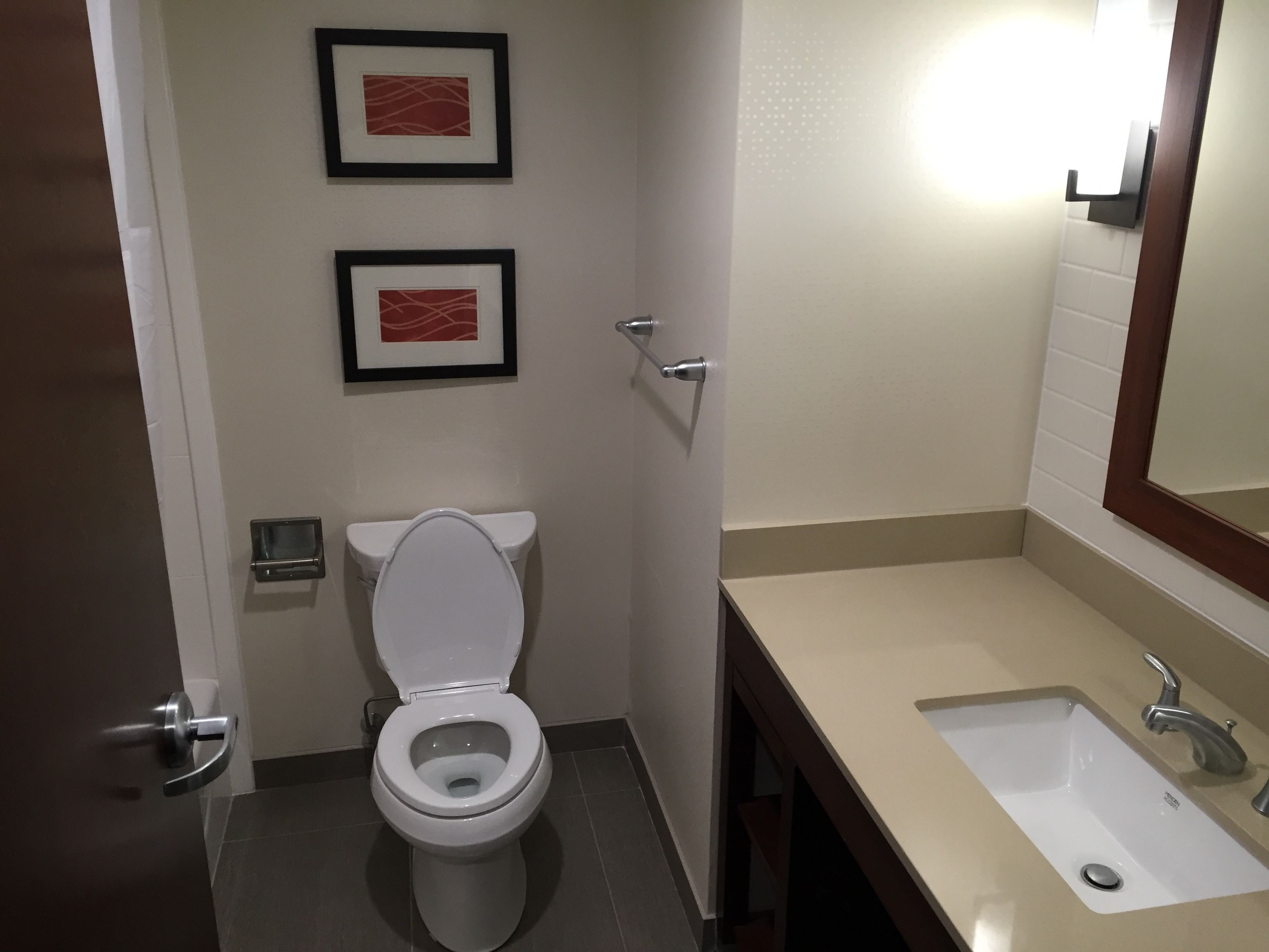 A bathroom with a toilet, sink, and two framed pictures on the wall.