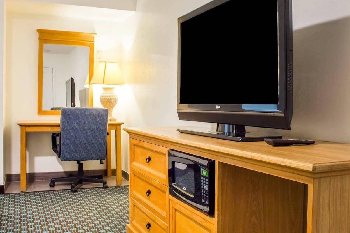 A hotel room with a wooden desk, a chair, a television, and a microwave.