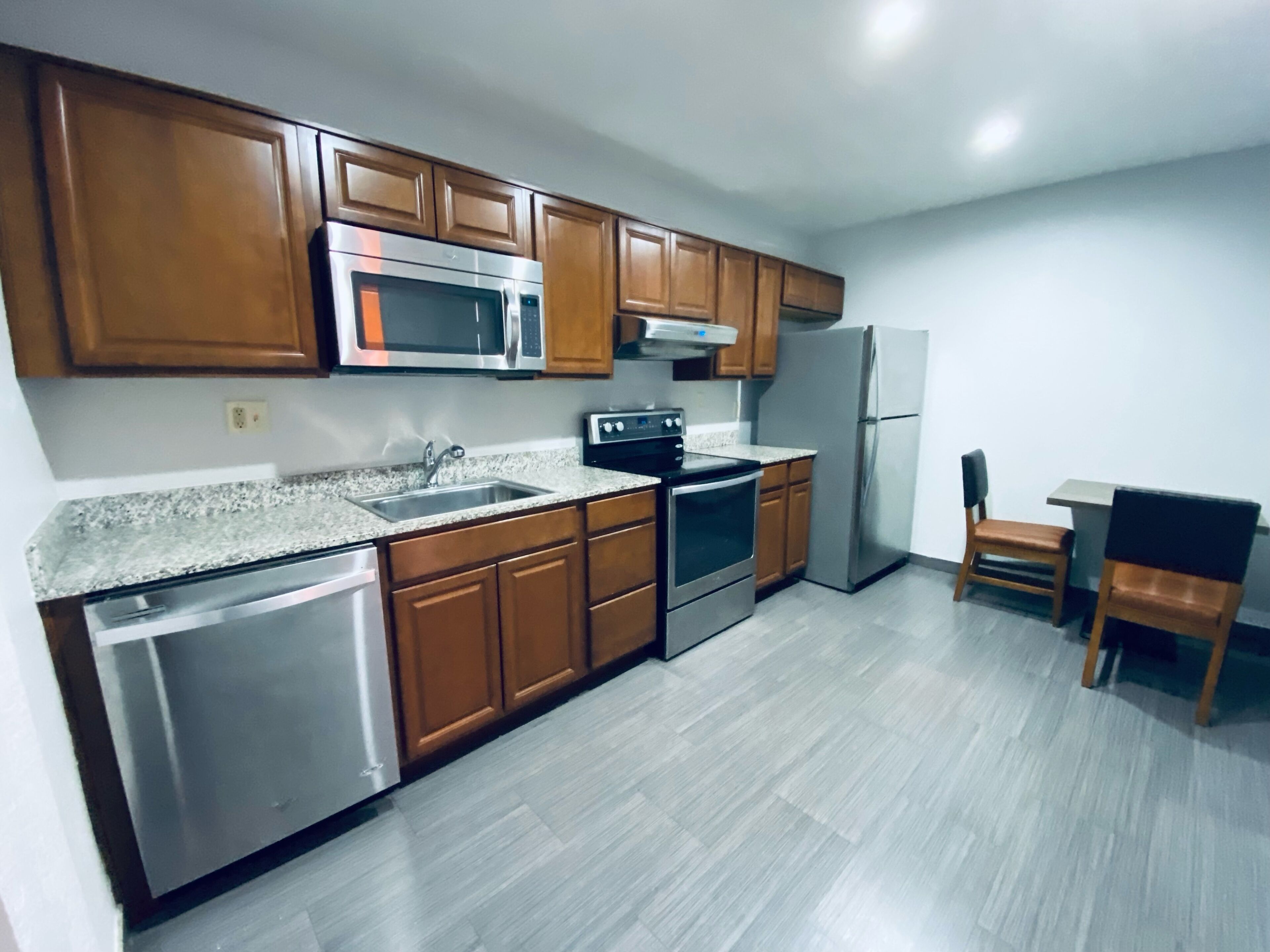 A kitchen with wooden cabinets, stainless steel appliances, a granite countertop, and a small dining area with a table and chairs.