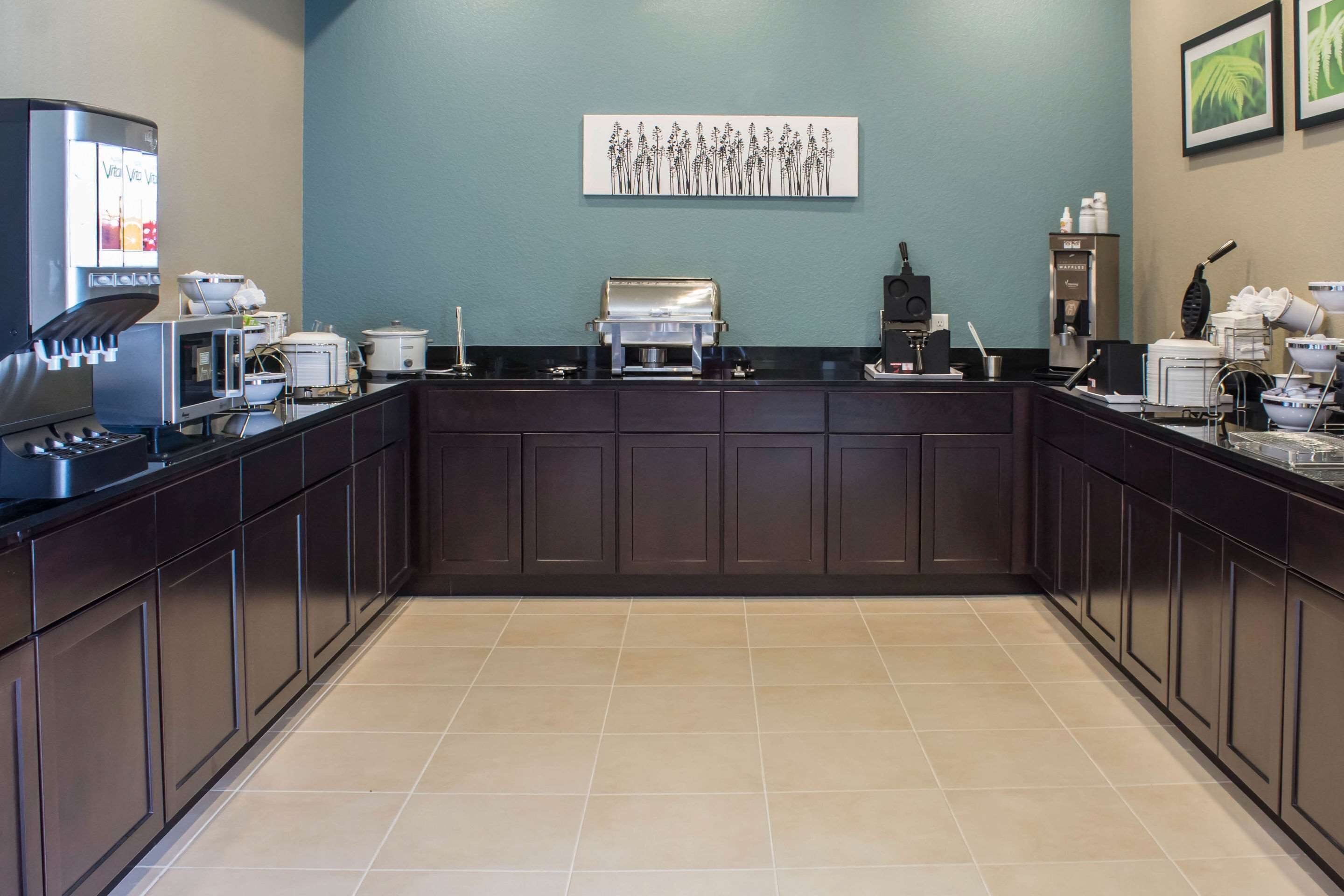 A modern kitchen with dark wooden cabinets, a large island, and various appliances including a coffee machine and microwave.