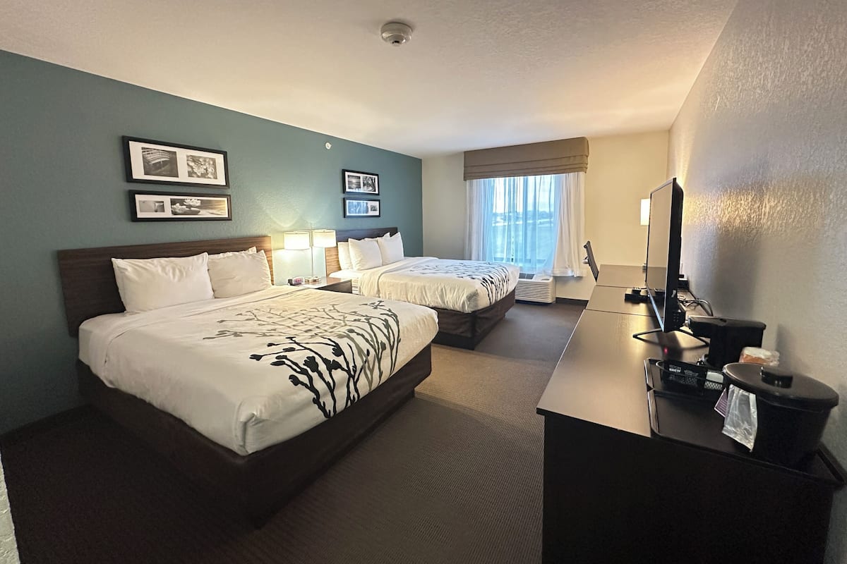 A hotel room with two beds, a desk, a TV, and a window with curtains.