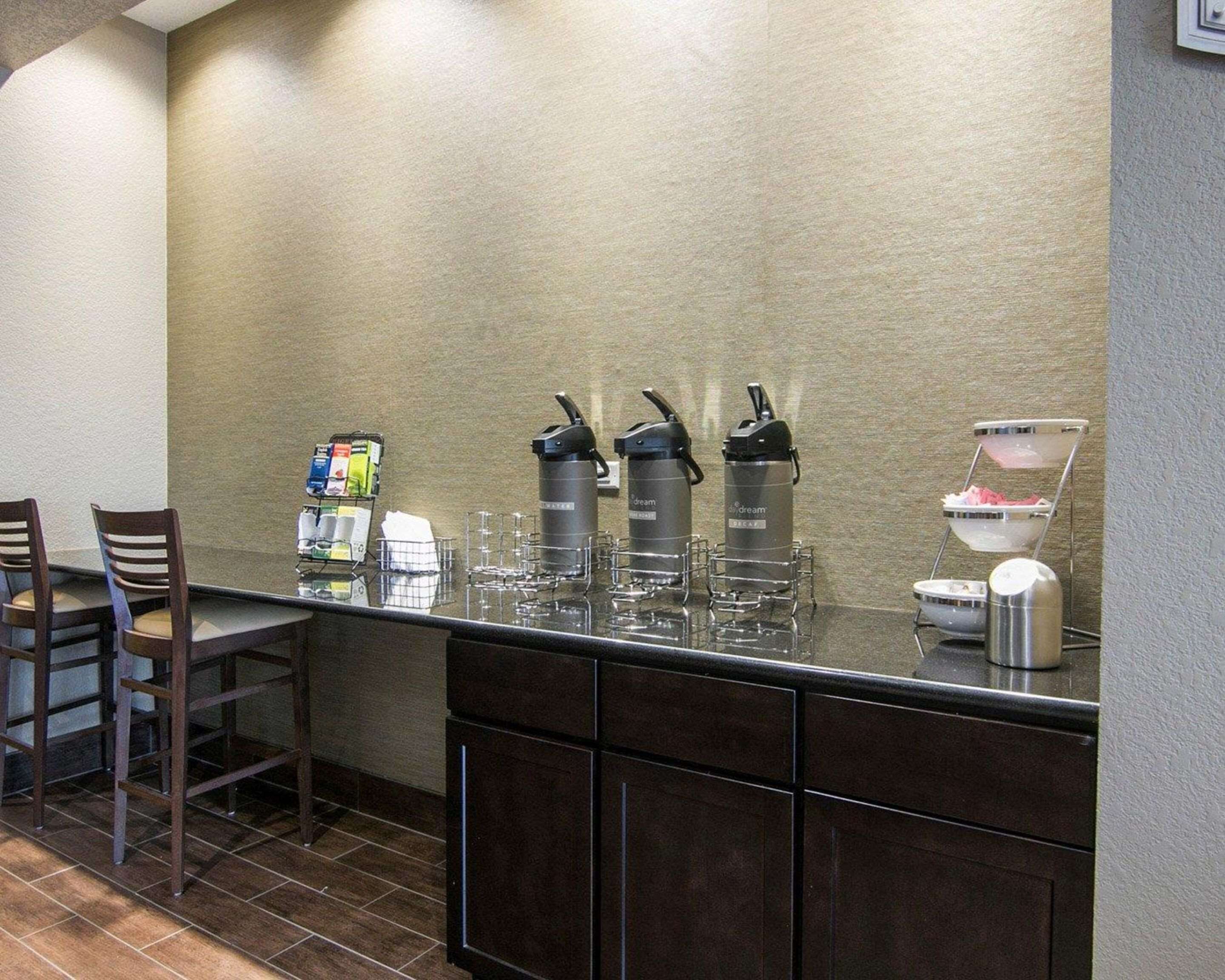 Een ontbijtbuffet met koffieautomaten, een drankenspender en een schaal fruit.