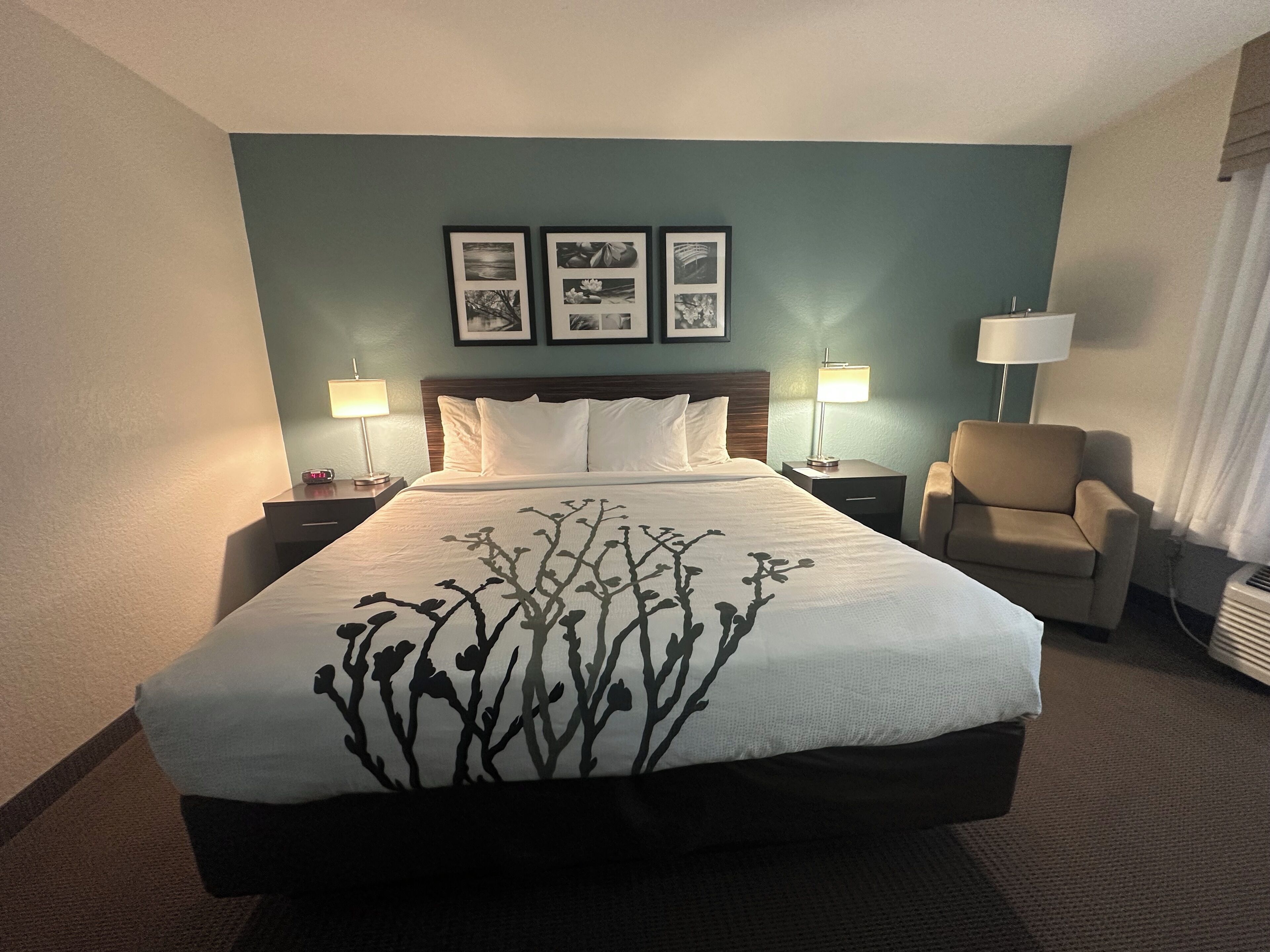 A hotel room with a large bed, two bedside tables with lamps, a chair, and three framed pictures on the wall.