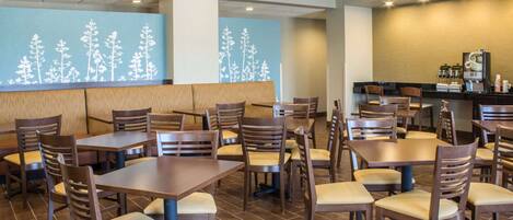 A restaurant with wooden tables and chairs, a counter with a coffee machine, and a wall with a tree mural.