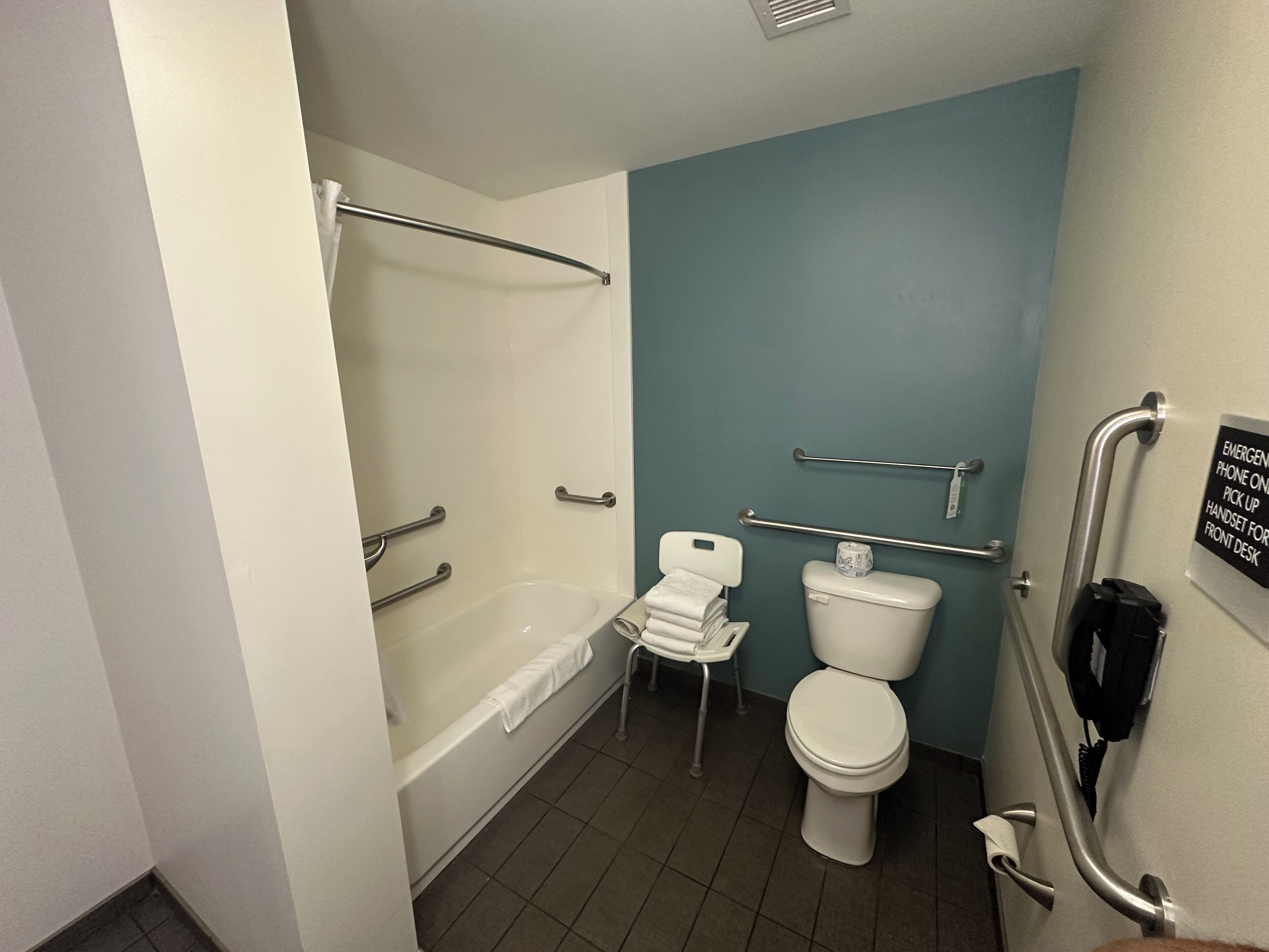 A bathroom with a bathtub, toilet, and handrails.