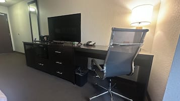 A hotel room with a desk, a chair, a television, and a lamp.