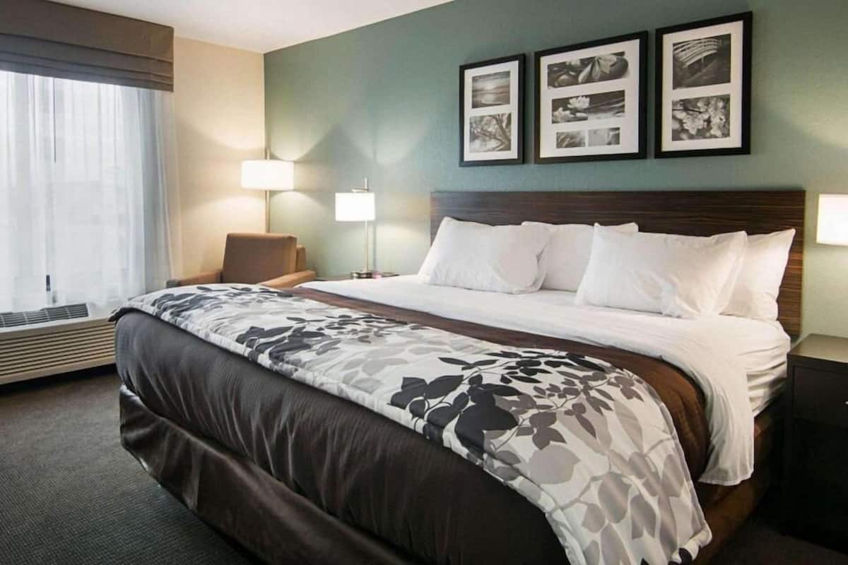 A hotel room with a large bed, two bedside lamps, a chair, and a window with curtains.