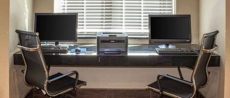 A workspace with two monitors, a printer, and two office chairs.