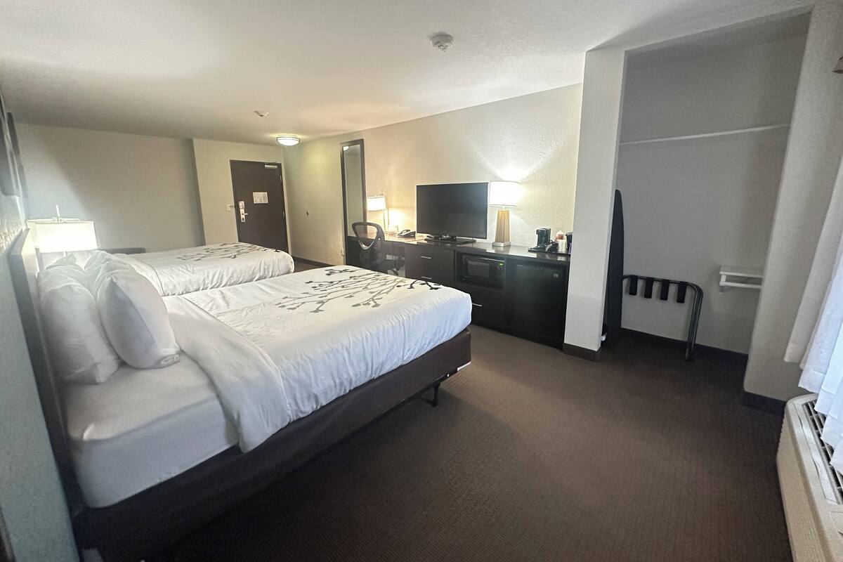 A hotel room with two beds, a desk with a computer, a TV, and a mirror.