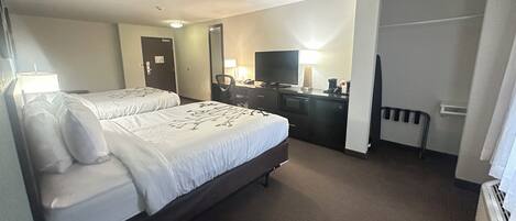 A hotel room with two beds, a desk with a computer, a TV, and a mirror.