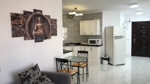 A modern kitchen with white cabinets, a microwave, and a refrigerator. There is a dining area with a glass table and chairs. - Regency Towers Apartments (Hurghada)