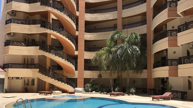 A multi-level building with a central pool, surrounded by potted plants and outdoor seating. - Regency Towers Apartments (Hurghada)
