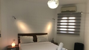 A neatly made bed with white linens and pillows, a bedside lamp, a wall-mounted air conditioner, and a window with blinds. - Regency Towers Apartments (Hurghada)