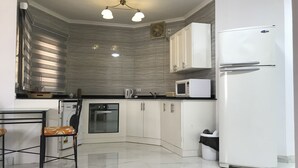 A compact kitchen with white cabinets, a microwave, a refrigerator, and a sink. - Regency Towers Apartments (Hurghada)
