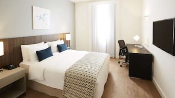Ein Hotelzimmer mit Bett, Nachttischen, Schreibtisch, Stuhl, Fernseher und einem Fenster mit Vorhängen.