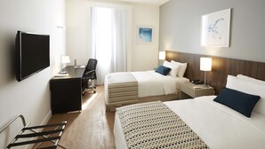 Hotellihuone, jossa on kaksi sänkyä, työpöytä, tuoli, televisio ja ikkuna, jossa on verhot.