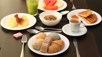 A breakfast table with plates of food, a glass of green juice, and a cup of coffee.