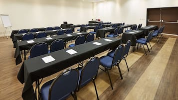 Un salón de conferencias con filas de mesas y sillas, una pizarra y un atril.