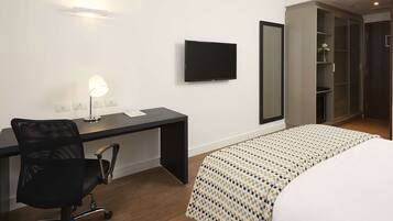 A hotel room with a bed, a desk with a chair, a TV, a mirror, and a wardrobe.