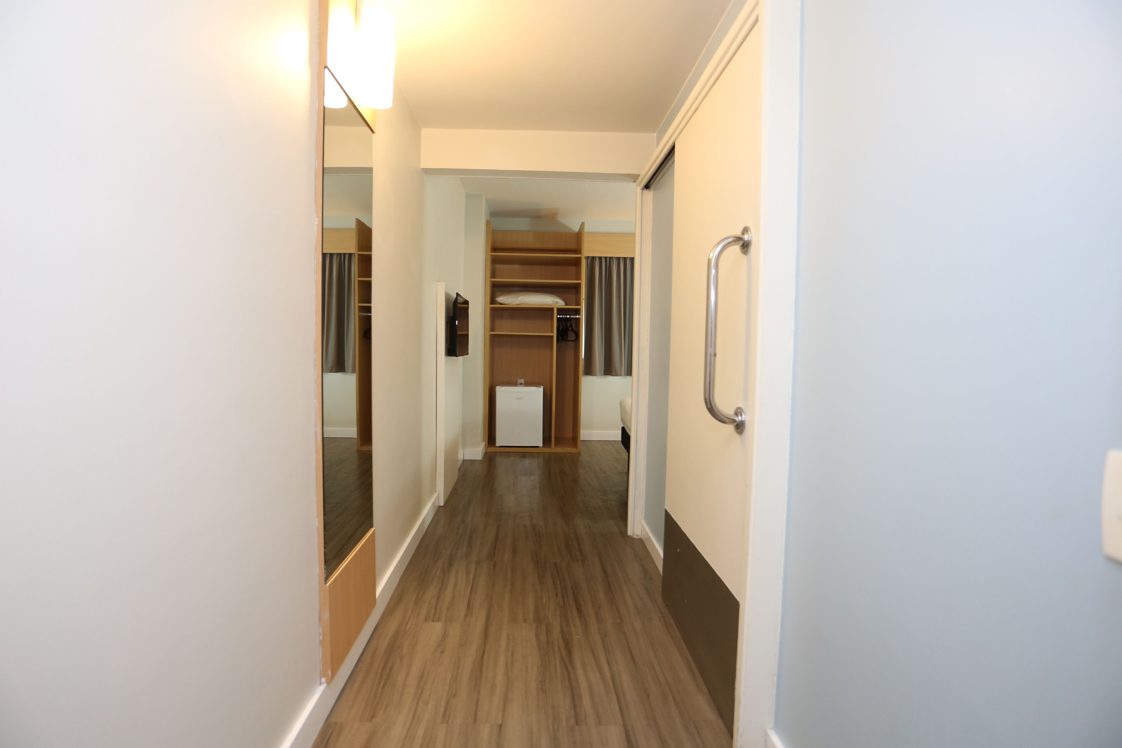 A narrow hallway with wooden flooring, a built-in closet with shelves, and a small refrigerator.