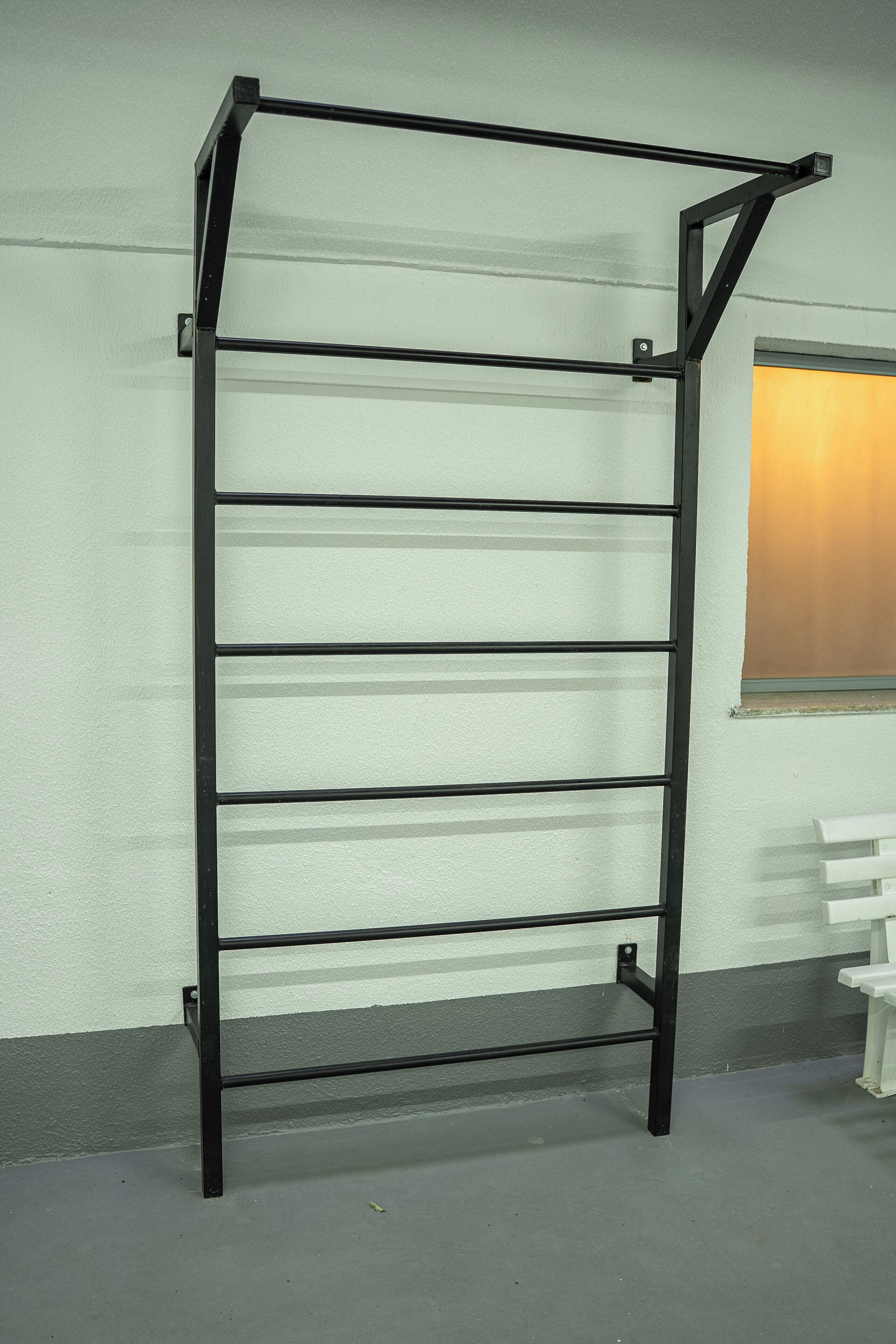A black metal rack with multiple shelves against a wall with a window.