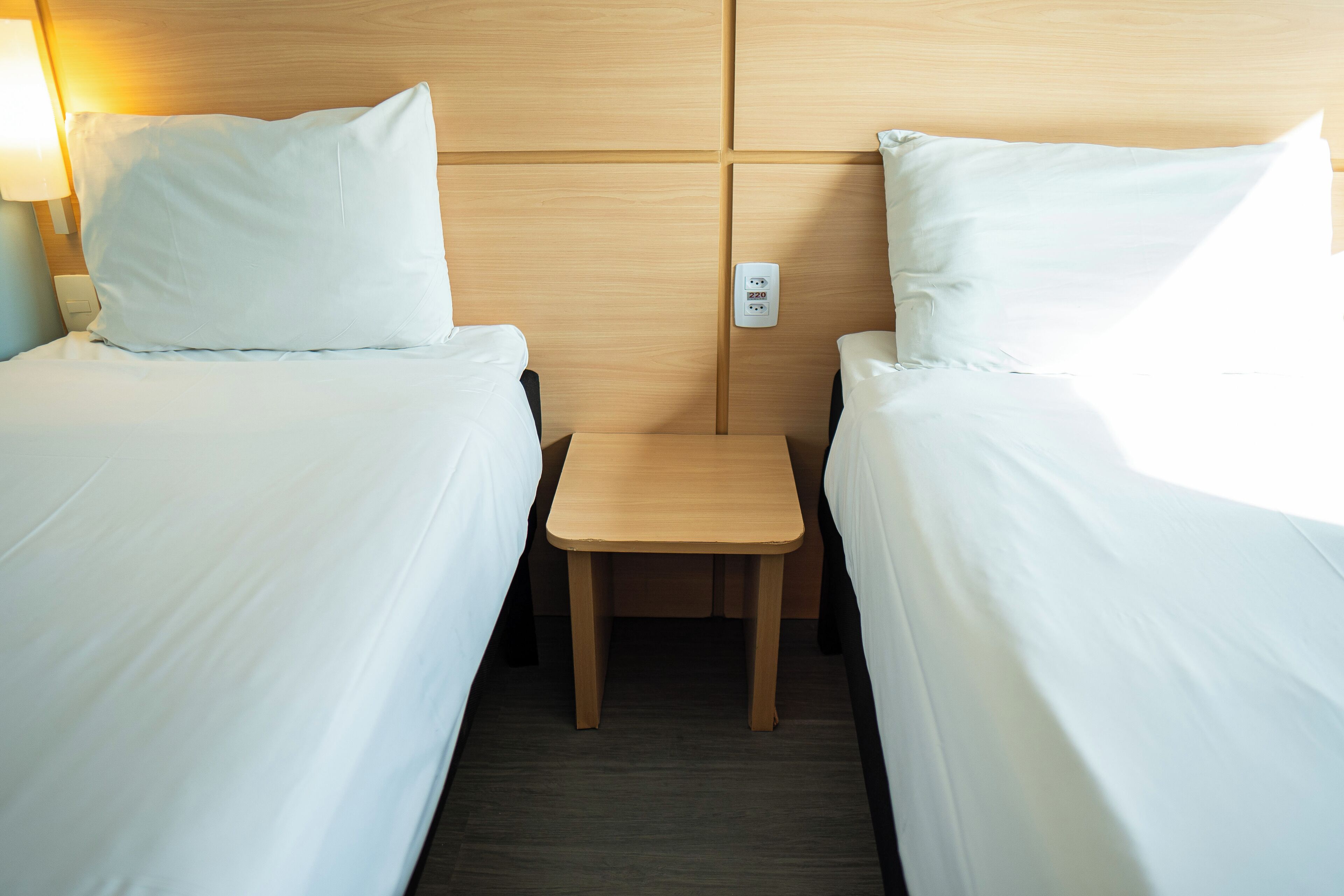 Une chambre d’hôtel avec deux lits simples, une table de chevet en bois et une petite table placée entre les lits.