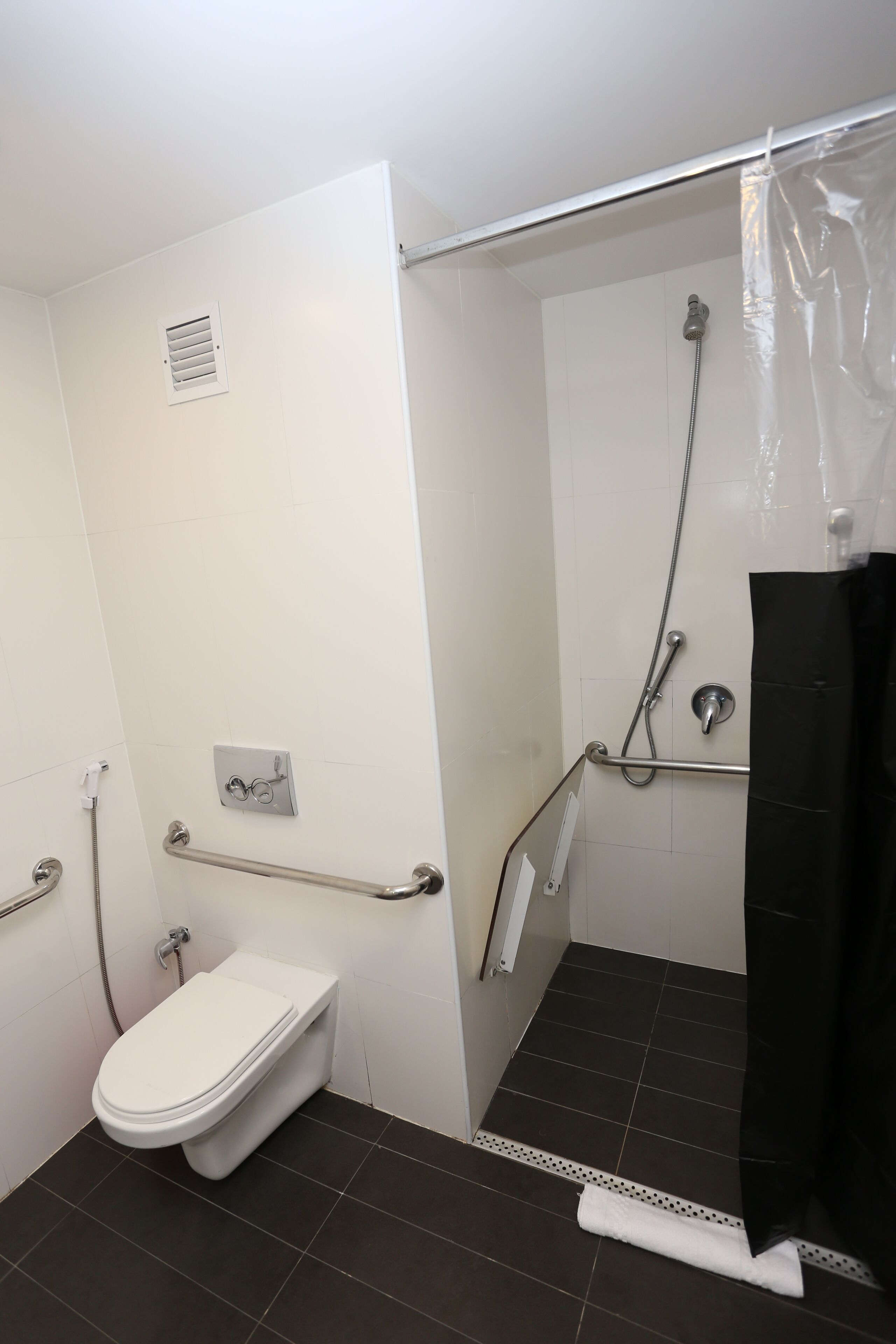 A bathroom with a toilet, a shower with a grab bar, and a black shower curtain.