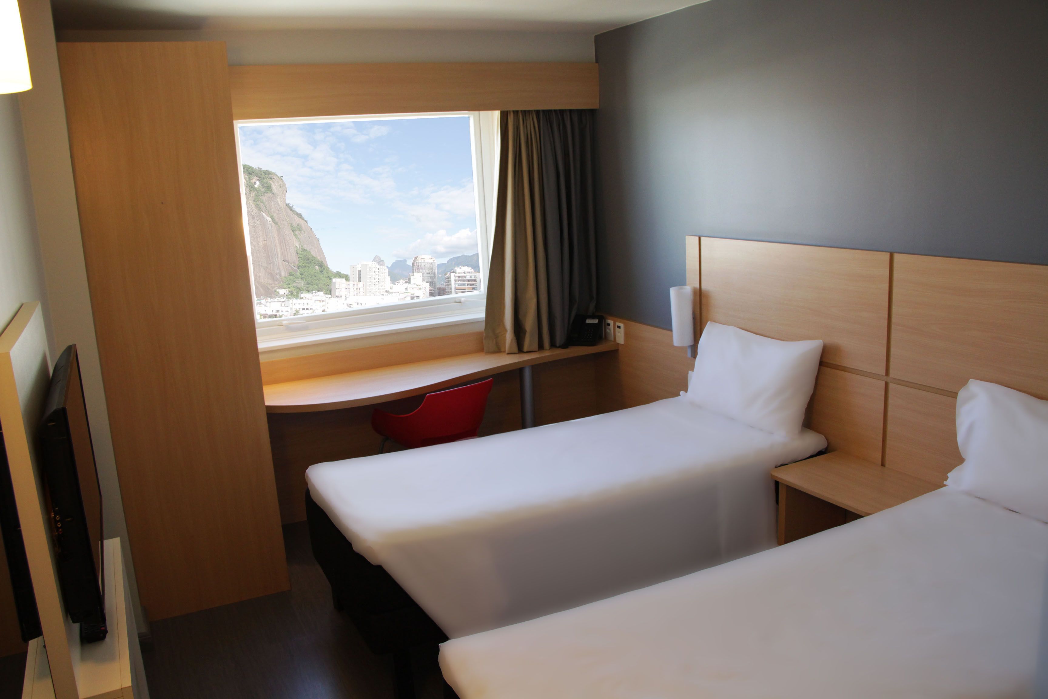 Une chambre d’hôtel avec deux lits, un bureau, une télévision et une fenêtre donnant sur la ville.