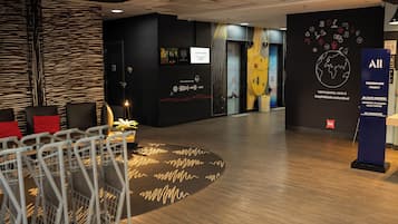 Un hall de hotel con mostrador de recepción, zona de estar y una pared con varios carteles y obras de arte.