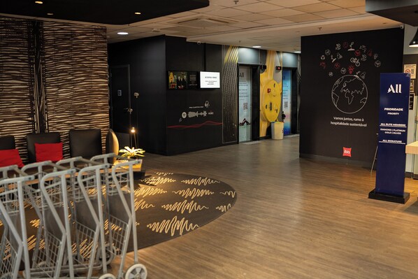 Un hall de hotel con mostrador de recepción, zona de estar y una pared con varios carteles y obras de arte.