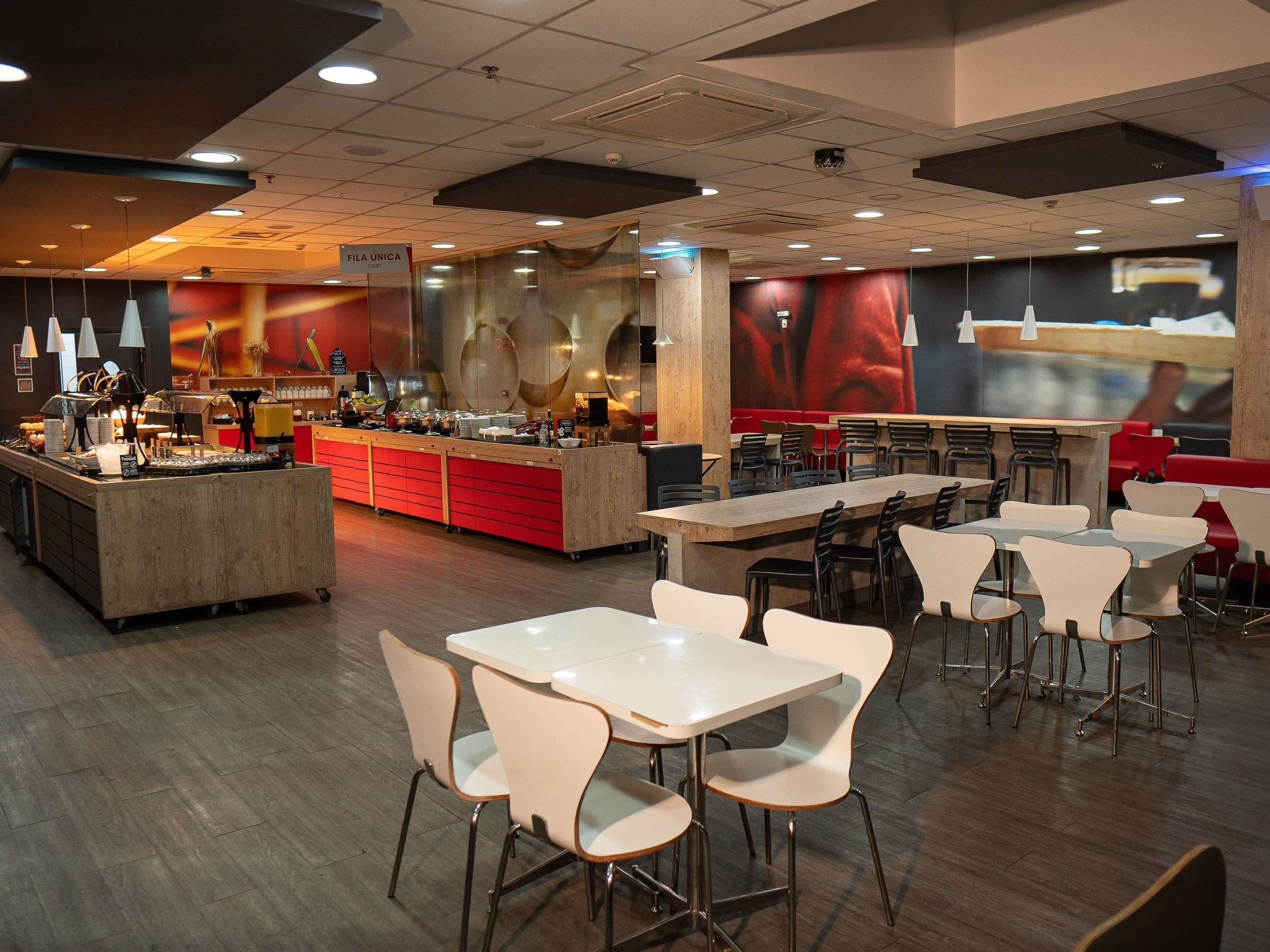 A modern cafeteria with a central serving station, multiple tables, and chairs.