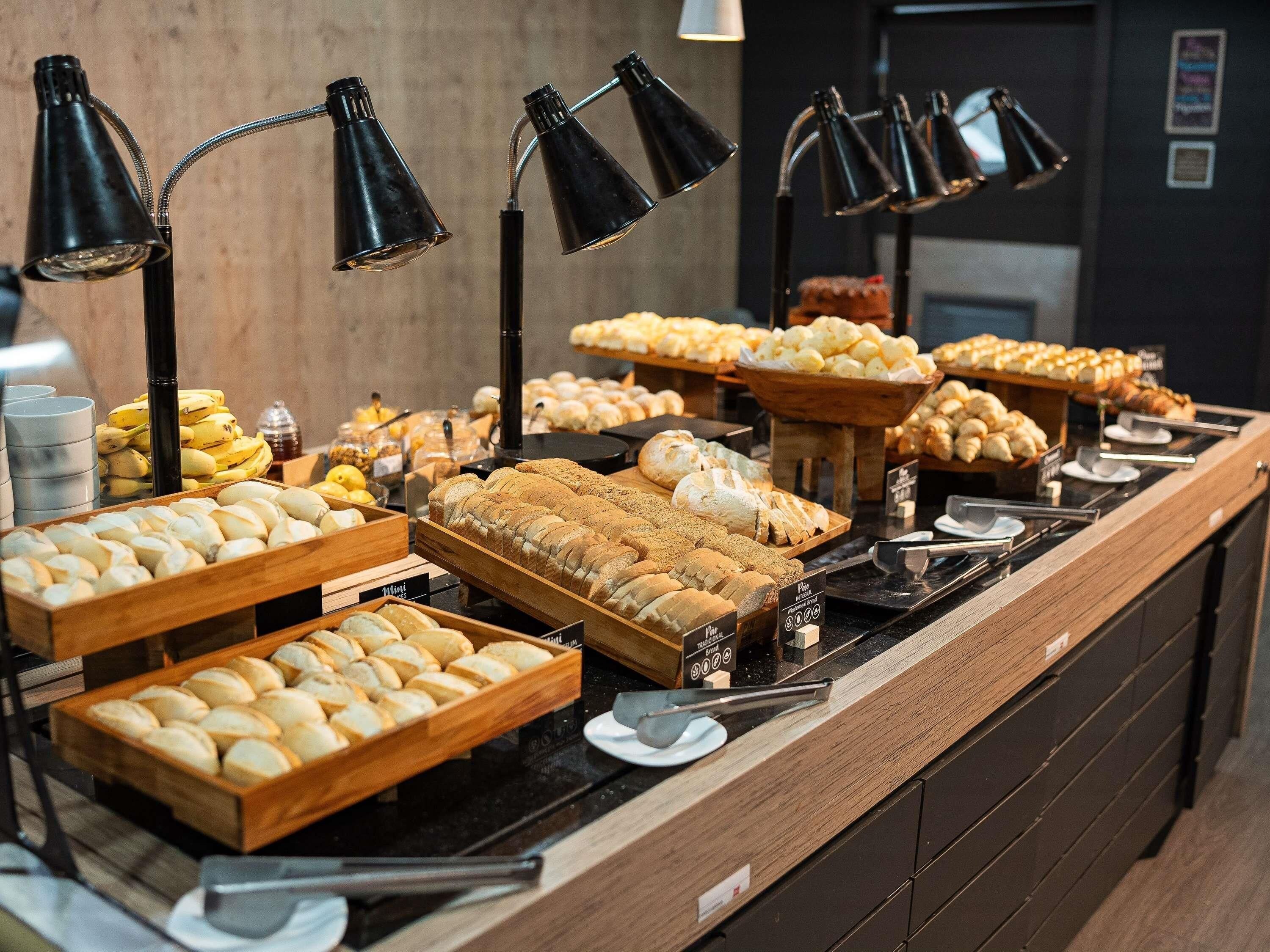 A buffet counter with various bread and pastries, accompanied by black lamps.