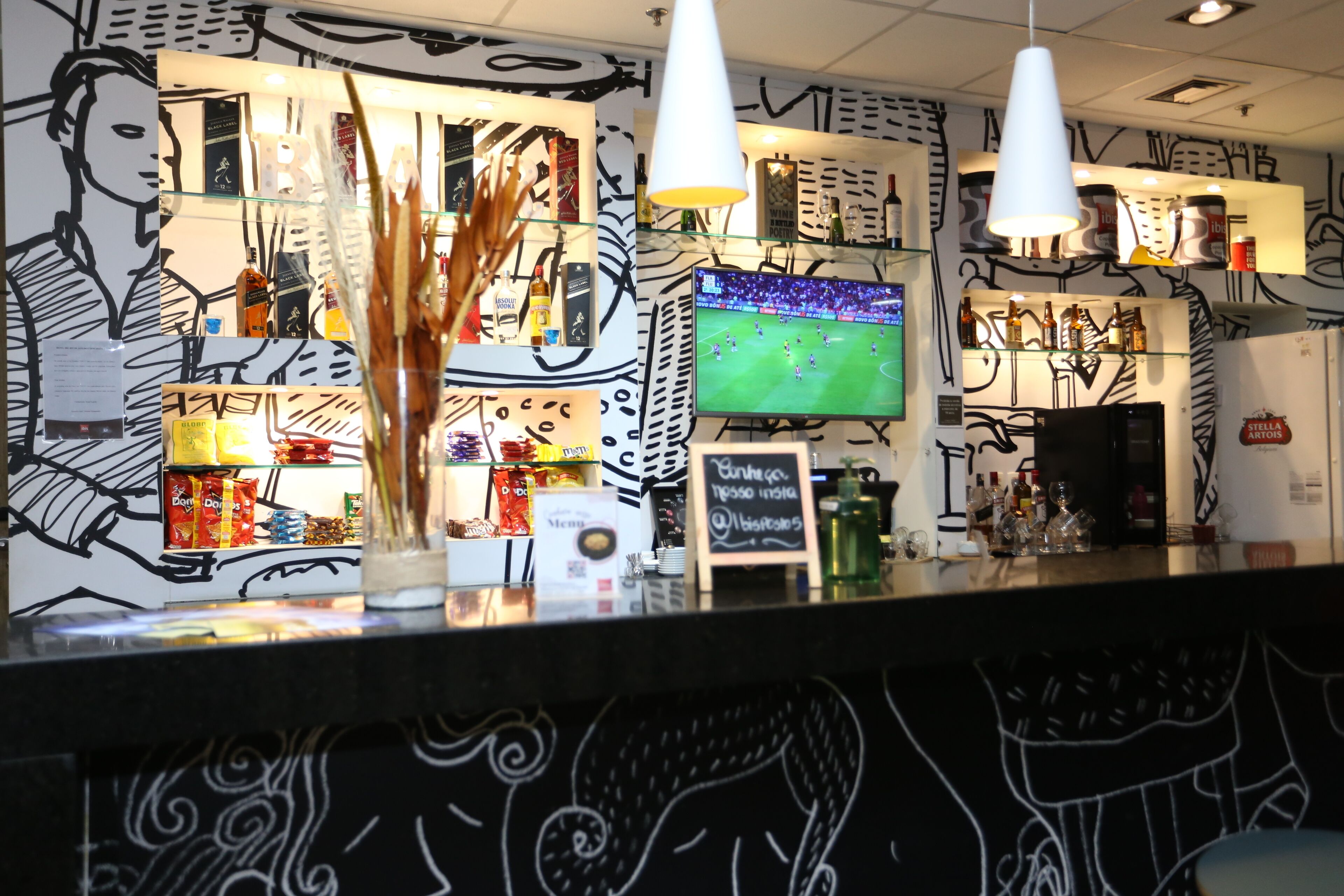 Zona de bar con una televisión mostrando un evento deportivo, estantes con botellas y un menú en la pizarra.