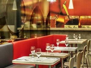 L’intérieur d’un restaurant avec des banquettes rouges, des tables blanches et des verres à vin.
